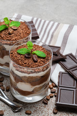 two portions Classic tiramisu dessert in a glass and chocolate bar on concrete background