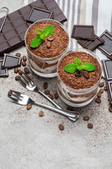 two portions Classic tiramisu dessert in a glass and chocolate bar on concrete background