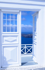 White wooden light open door. Behind the door is a beautiful turquoise sea and mountains. Sunny morning on the Greek island of Santorini.