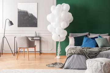 Bunch of white balloons in elegant grey and green bedroom interior with king size bed with grey...