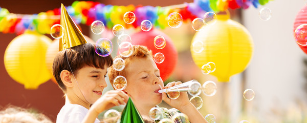 Boys playing with soap bubbles during birthday party for children - Powered by Adobe