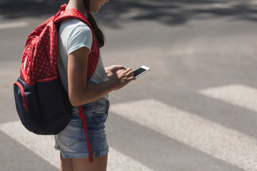 Teenage schoolgirl with backpack using phone during her way from school