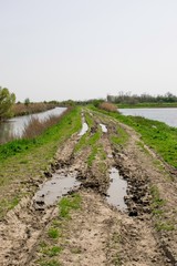 Fototapeta premium Muddy village road with puddle and water on both sides