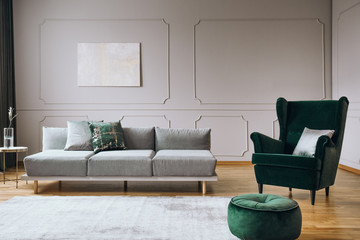 Elegant living room interior with emerald green chair with pillow and long grey couch