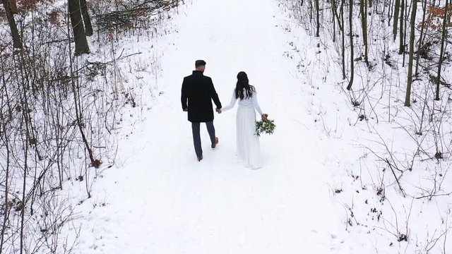 View of striding newlyweds bride and groom holding wedding bouquet from aerial view.
