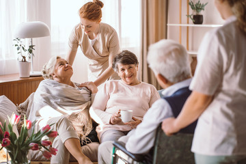 Young caregiver comforting elderly woman in nursing home - obrazy, fototapety, plakaty