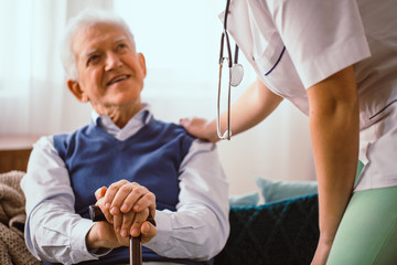 Elderly man with walking stick being comforted by doctor in nursing home