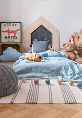 Pouf on striped rug in child's bedroom interior with teddy bear next to blue bed and poster. Real...