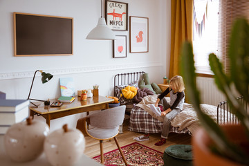 Blonde kid putting shoes on in vintage style bedroom