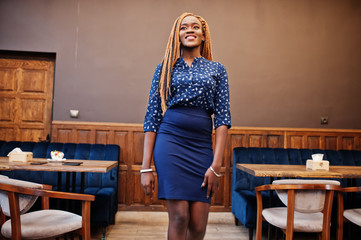Portrait of beautiful young african business woman with dreadlocks, wear on blue blouse and skirt, posed in cafe.