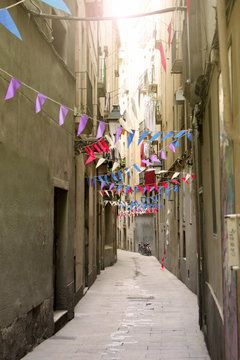 Menschenleere, schmale Gasse geschm&uuml;ckt mit bunten Girlanden in Barcelona