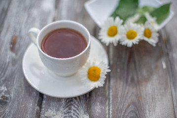 Tea in a white cup on a wooden table. Daisies on the table