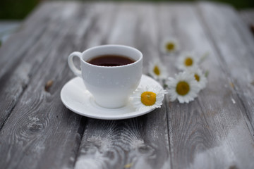 Tea in a white cup on a wooden table. Daisies on the table