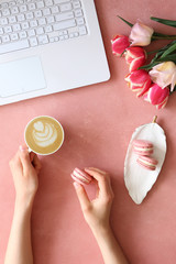 Top view shot of woman typing on white laptop computer, concrete textured table background. Feminine workspace with flowers bouquet. Close up, copy space.
