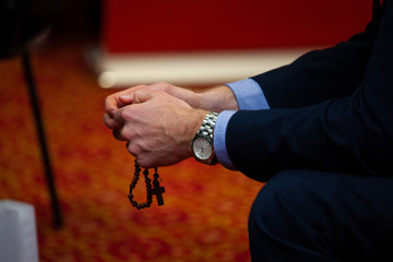 Man praying holding a rosary in his hands with wooden beads