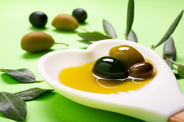 in the foreground, in the heart-shaped white spoon some olives with extra virgin olive oil