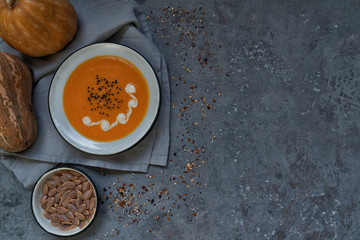 Bowl of pumpkin organic soup with cream and pumpkin seeds on gray background. Dietary vegetarian food. Concept of healthy eating food. Homemade autumn soup. Top view with copy space. Toned image.