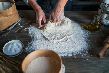Female hands making dough for pizza. Baker kneading fresh raw dough on kitchen table. Concept of...
