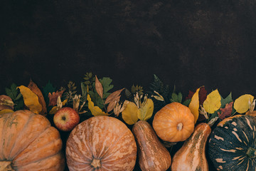 Fresh autumn seasonal vegetables and fruits on brown old background. Fallen leaves, red apples,...