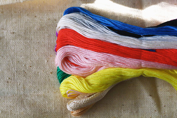 multi-colored colorful raindow colors threads for embroidery floss on light fabric canvas close-up,...