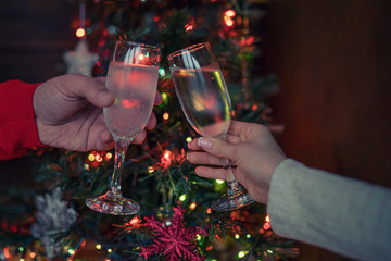 Two glasses of champagne raised in a toast against a Christmas tree glowing lights. Holiday and togetherness a family Christmas and Happy New Year. Party time. Couple with champagne. Selective focus.