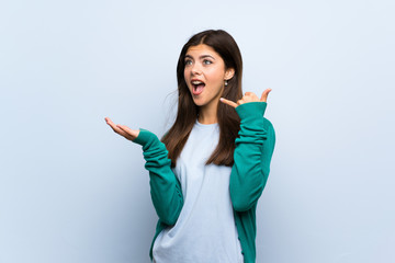 Teenager girl over blue wall making phone gesture and doubting