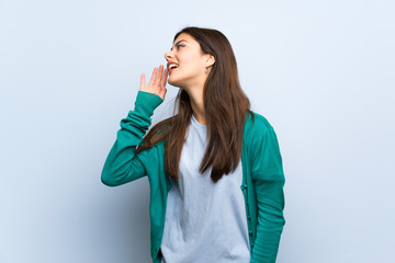 Teenager girl over blue wall listening to something by putting hand on the ear