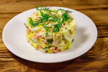 Salad with crab sticks, sweet corn, cucumber, eggs and mayonnaise on wooden table