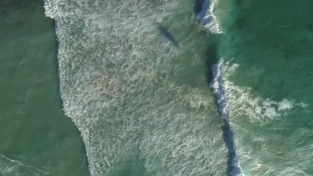 Aerial view of ocean waves. Top down view. Windsrufer fighting waves. People riding windboard and kiteboard. Cape Town, South Africa. Aerial footage.