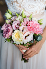 Unrecognizable bride holding a refined wedding bouquet of white and pink roses with eustoma