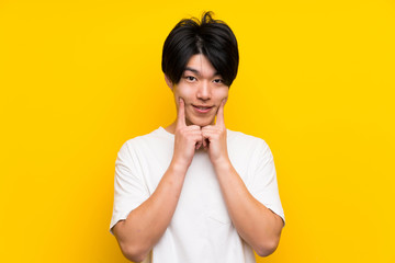 Asian man over isolated yellow wall smiling with a happy and pleasant expression
