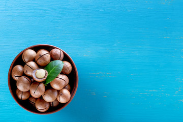 Australian macadamia nuts with leaf in plate on blue wooden background