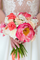 Unrecognizable bride holding a refined wedding bouquet of pink and red roses with peonies