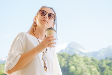 Stylish woman with cup of coffee on background of summer mountains.