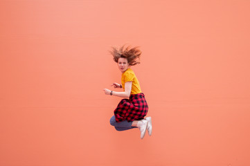 young stylish girl jumping on a coral background, dancing and having fun