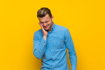 Blonde man over isolated yellow wall with toothache