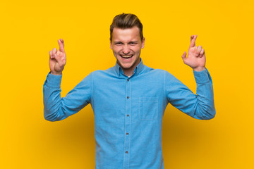 Fototapeta premium Blonde man over isolated yellow wall with fingers crossing