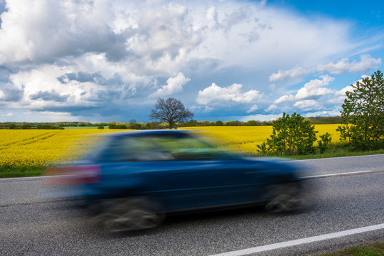 Blaues Auto f&auml;hrt rasch durch gelbe Rapsfelder, Schleswig-Holstein