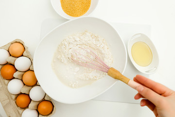 Baking ingredients closeup. Eggs sugar and oil on the table. Flour, and milk in a bowl with a whisk. Flat lay view.