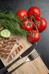 Greens with tomatoes and grilled Turkey steak on a chopping Board. Cutlery on a cutting Board. Top view