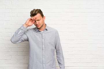 Blonde man over white brick wall with tired and sick expression