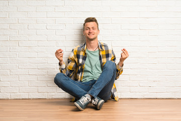 Blonde man sitting on the floor making money gesture