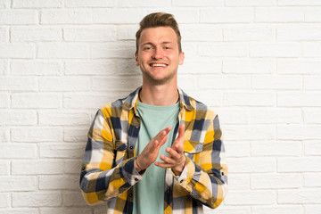 Blonde handsome man over white brick wall applauding