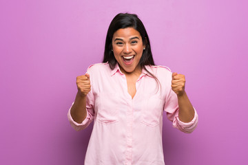 Young Colombian girl over purple wall celebrating a victory in winner position