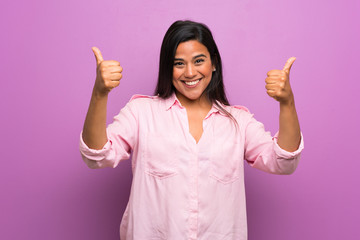 Young Colombian girl over purple wall with thumbs up gesture and smiling