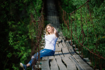 Naklejka na ściany i meble Beautiful Girl i sitting on old wooden bridge. Travel and Vacation in the park.Young blonde woman relaxing of green trees in the park. girl enjoys outdoor recreation in the spring.
