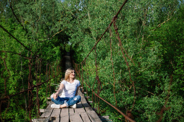 Beautiful Girl i sitting on  old  wooden bridge. Travel and Vacation in the park.Young blonde woman relaxing of green trees in the park. girl enjoys outdoor recreation in the spring.