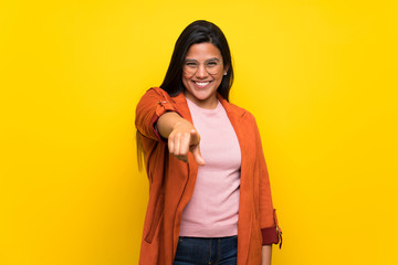 Young Colombian girl over yellow wall points finger at you with a confident expression