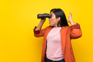 Young Colombian girl over yellow wall and looking in the distance with binoculars