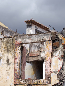close up of the windows of a collapsing abandoned roofless house with broken shutter and grey sky